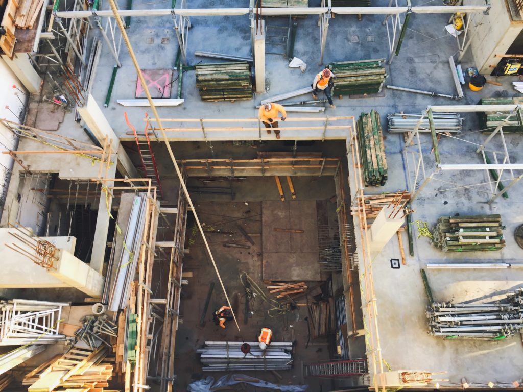 https://www.newangledrone.com/wp-content/uploads/2023/07/looking-down-at-a-construction-site-with-workers-busy-building.jpg